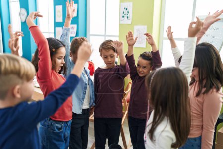 Téléchargez les photos : Groupe d'élèves souriants confiants avec les mains levées en classe - en image libre de droit