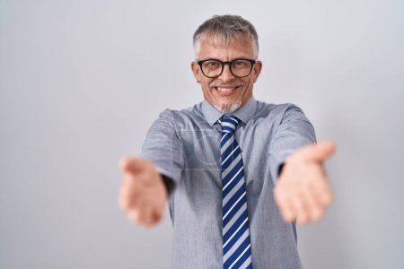 Téléchargez les photos : Homme d'affaires hispanique aux cheveux gris portant des lunettes souriant gai offrant des mains donnant assistance et acceptation. - en image libre de droit