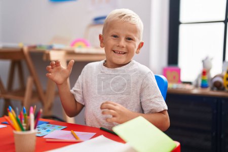 Photo for Little caucasian boy painting at the school celebrating achievement with happy smile and winner expression with raised hand - Royalty Free Image