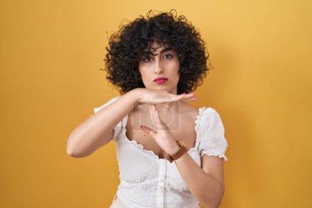 Téléchargez les photos : Jeune femme brune aux cheveux bouclés debout sur fond jaune faisant un geste avec les mains, frustré et sérieux visage - en image libre de droit
