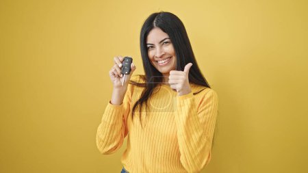 Photo for Young beautiful hispanic woman holding key of new car doing ok gesture over isolated yellow background - Royalty Free Image