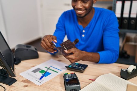 Téléchargez les photos : Jeune homme afro-américain commerce électronique travailleur d'affaires tenant portefeuille avec carte de crédit au bureau - en image libre de droit