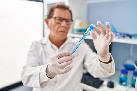 Téléchargez les photos : Middle age man wearing scientist uniform looking test tube at laboratory - en image libre de droit