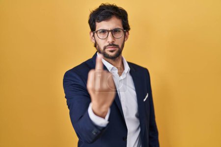 Foto de Handsome latin man standing over yellow background showing middle finger, impolite and rude fuck off expression - Imagen libre de derechos