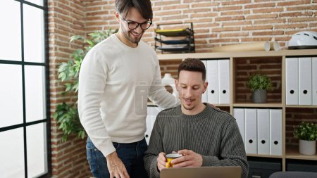 Téléchargez les photos : Deux hommes partenaires commerciaux utilisant un ordinateur portable boire du café au bureau - en image libre de droit