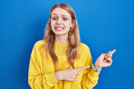 Photo for Young caucasian woman standing over blue background pointing aside worried and nervous with both hands, concerned and surprised expression - Royalty Free Image