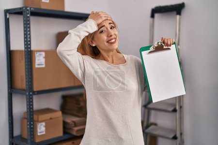 Photo for Hispanic woman working at small business ecommerce holding clipboard with blank space stressed and frustrated with hand on head, surprised and angry face - Royalty Free Image