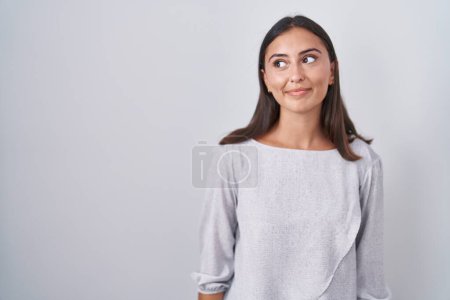 Foto de Mujer hispana joven de pie sobre fondo blanco sonriendo mirando hacia un lado y mirando hacia otro pensando. - Imagen libre de derechos