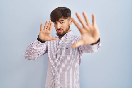 Téléchargez les photos : Homme arabe avec barbe debout sur fond bleu faisant cadre en utilisant les mains paumes et les doigts, perspective de la caméra - en image libre de droit