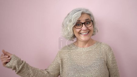 Foto de Middle age woman with grey hair smiling confident pointing to the side over isolated pink background - Imagen libre de derechos