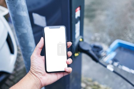 Téléchargez les photos : Man holding smartphone showing white blank screen at electrical car station - en image libre de droit