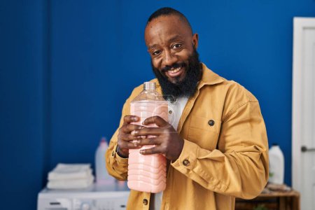 Téléchargez les photos : Young african american man smilng confident smelling detergent at laundry room - en image libre de droit