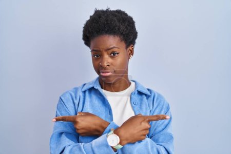 Téléchargez les photos : Femme afro-américaine debout sur fond bleu pointant des deux côtés avec les doigts, direction différente en désaccord - en image libre de droit