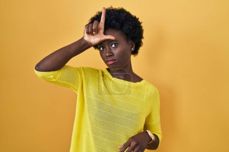 Téléchargez les photos : Jeune femme africaine debout sur le studio jaune se moquant des gens avec les doigts sur le front faisant geste perdant moquerie et insultant. - en image libre de droit