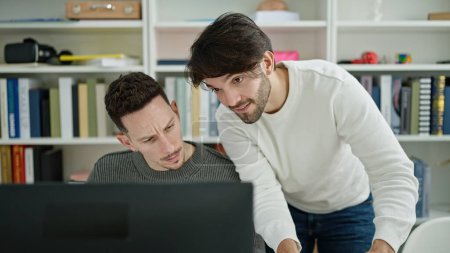 Téléchargez les photos : Deux étudiants hommes utilisant l'ordinateur étudient à la bibliothèque universitaire - en image libre de droit