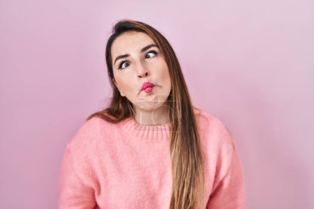 Photo for Young hispanic woman standing over pink background making fish face with lips, crazy and comical gesture. funny expression. - Royalty Free Image