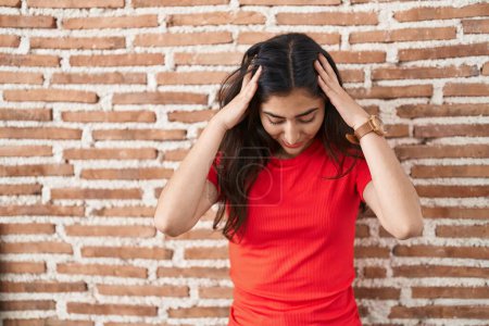Foto de Joven adolescente de pie sobre la pared de ladrillos que sufren de dolor de cabeza desesperada y estresada porque el dolor y la migraña. manos en la cabeza. - Imagen libre de derechos