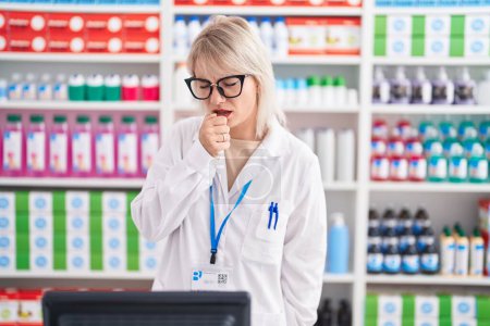 Téléchargez les photos : Jeune femme caucasienne travaillant à la pharmacie se sentant mal et toussant comme symptôme du rhume ou de la bronchite. concept de soins de santé. - en image libre de droit