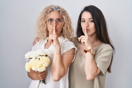 Téléchargez les photos : Mère et fille tenant un bouquet de fleurs blanches demandant à se taire avec le doigt sur les lèvres. silence et concept secret. - en image libre de droit