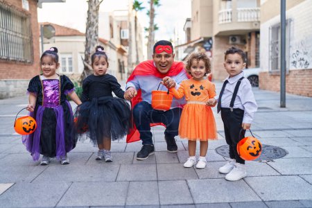 Foto de Hombre hispano y grupo de niños con disfraz de halloween sonriendo en la calle - Imagen libre de derechos