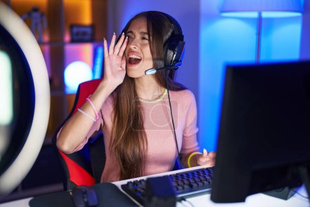 Photo for Young hispanic woman playing video games shouting and screaming loud to side with hand on mouth. communication concept. - Royalty Free Image