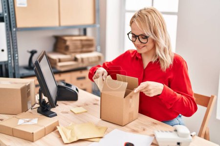 Téléchargez les photos : Jeune femme blonde commerce électronique entreprise emballage boîte en carton au bureau - en image libre de droit