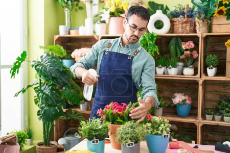 Téléchargez les photos : Young hispanic man florist using diffuser watering plant at flower shop - en image libre de droit