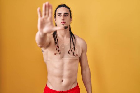 Photo for Hispanic man with long hair standing shirtless over yellow background doing stop sing with palm of the hand. warning expression with negative and serious gesture on the face. - Royalty Free Image