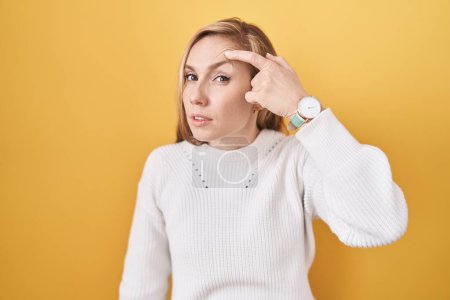 Photo for Young caucasian woman wearing white sweater over yellow background pointing unhappy to pimple on forehead, ugly infection of blackhead. acne and skin problem - Royalty Free Image