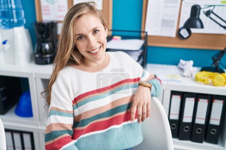 Photo for Young blonde woman business worker smiling confident sitting on table at office - Royalty Free Image