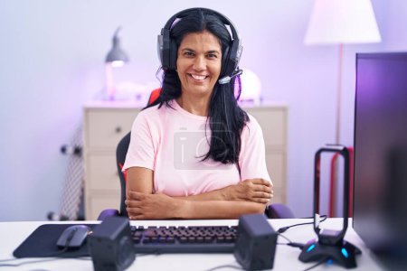 Téléchargez les photos : Femme hispanique mature jouant à des jeux vidéo à la maison visage heureux souriant avec les bras croisés en regardant la caméra. personne positive. - en image libre de droit