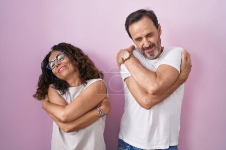 Téléchargez les photos : Couple hispanique du moyen âge ensemble sur fond rose se serrant dans ses bras heureux et positifs, souriant confiant. amour de soi et soins de soi - en image libre de droit