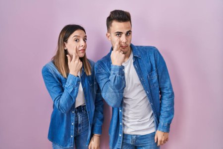 Photo for Young hispanic couple standing over pink background pointing to the eye watching you gesture, suspicious expression - Royalty Free Image