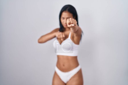 Photo for Hispanic woman wearing lingerie punching fist to fight, aggressive and angry attack, threat and violence - Royalty Free Image