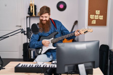 Foto de Young redhead man musician playing electrical guitar at music studio - Imagen libre de derechos