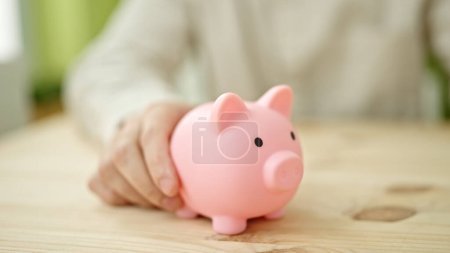 Photo for Young hispanic man holding piggy bank on table - Royalty Free Image