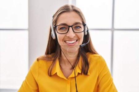 Foto de Mujer joven que usa auriculares de agente de centro de llamadas que se ven positivos y felices de pie y sonriendo con una sonrisa segura que muestra los dientes - Imagen libre de derechos