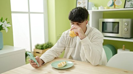 Photo for Young hispanic man using smartphone having breakfast at dinning room - Royalty Free Image