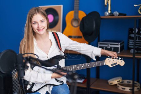 Foto de Joven mujer caucásica artista sonriendo confiado tocando guitarra eléctrica en el estudio de música - Imagen libre de derechos