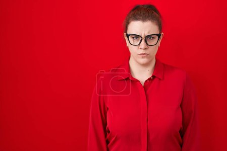 Photo for Young hispanic woman with red hair standing over red background skeptic and nervous, frowning upset because of problem. negative person. - Royalty Free Image