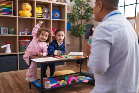 Photo for Hispanic man with boy and girl playing with vocabulary game standing at kindergarten - Royalty Free Image
