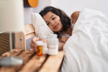Téléchargez les photos : Jeune femme couchée sur le lit tenant bouteille de pilules à la chambre - en image libre de droit