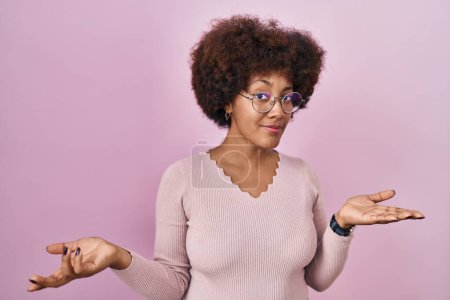 Téléchargez les photos : Jeune femme afro-américaine debout sur fond rose désemparé et confus avec les bras ouverts, aucune idée concept. - en image libre de droit