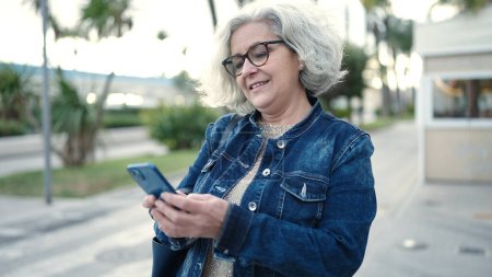 Téléchargez les photos : Middle age woman with grey hair using smartphone at street - en image libre de droit