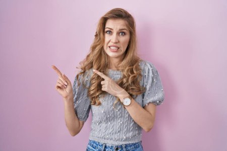 Photo for Beautiful blonde woman standing over pink background pointing aside worried and nervous with both hands, concerned and surprised expression - Royalty Free Image