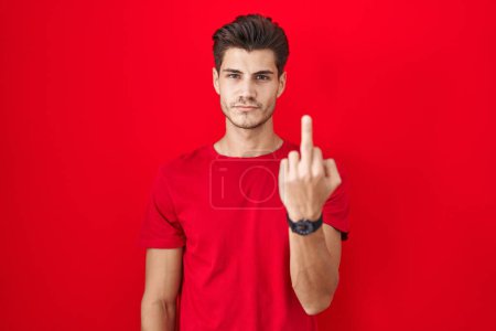 Foto de Young hispanic man standing over red background showing middle finger, impolite and rude fuck off expression - Imagen libre de derechos