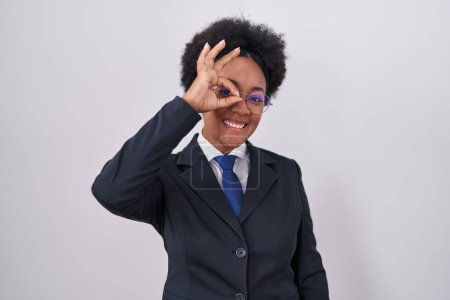 Photo for Beautiful african woman with curly hair wearing business jacket and glasses doing ok gesture with hand smiling, eye looking through fingers with happy face. - Royalty Free Image