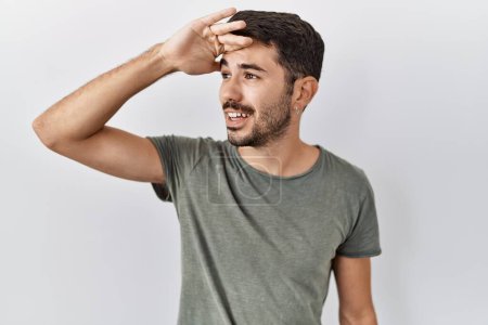 Photo for Young hispanic man with beard wearing casual t shirt over white background very happy and smiling looking far away with hand over head. searching concept. - Royalty Free Image