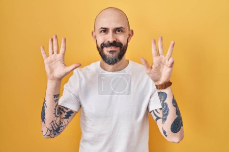 Téléchargez les photos : Young hispanic man with tattoos standing over yellow background showing and pointing up with fingers number nine while smiling confident and happy. - en image libre de droit