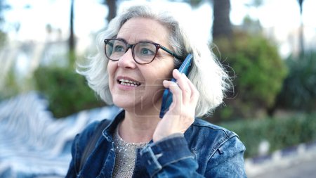 Téléchargez les photos : Middle age woman with grey hair speaking on the phone at park - en image libre de droit